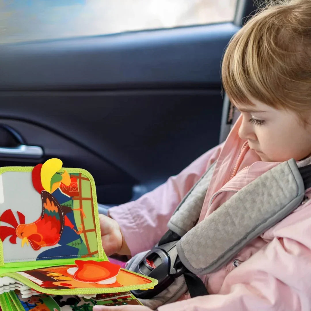 Copil în mașină explorând cu atenție paginile interactive ale cărții senzoriale Kinderspeech „Az én első farmom”, o jucărie educativă moale și ușoară, perfectă pentru a menține micuții ocupați în timpul călătoriilor